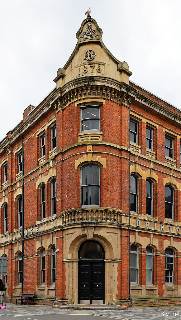 Entrance corner of the Brinton House built with red bricks and stones, with the build date 1876 written on the top of the building