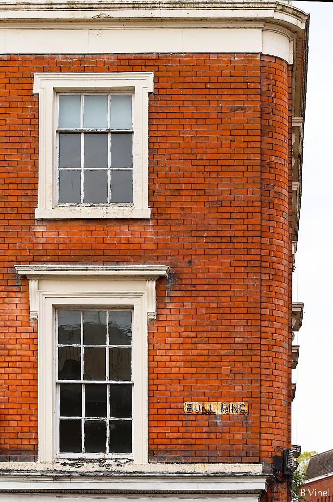 The corner of a red brick house with two white sash windows and a Bull Ring street sign