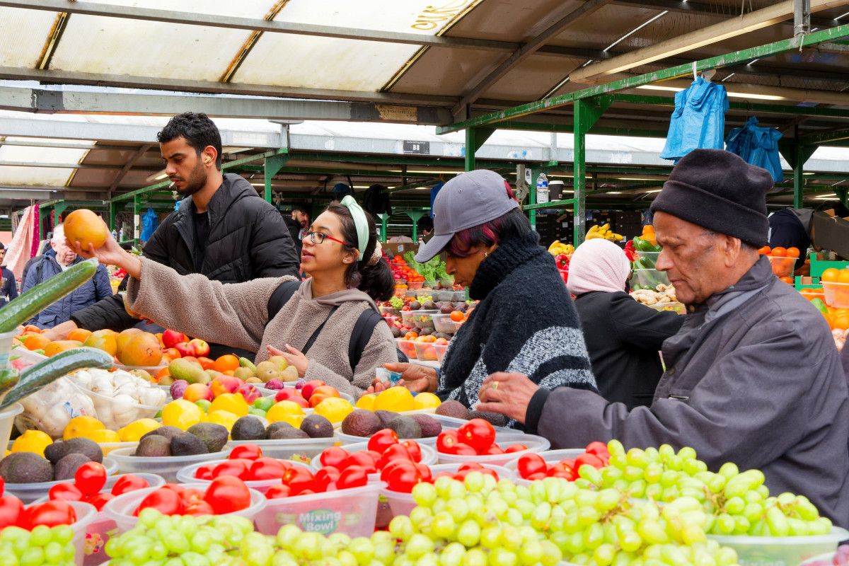 Customers are looking and buying fruits and vegetables in front of the market stale full of colours.