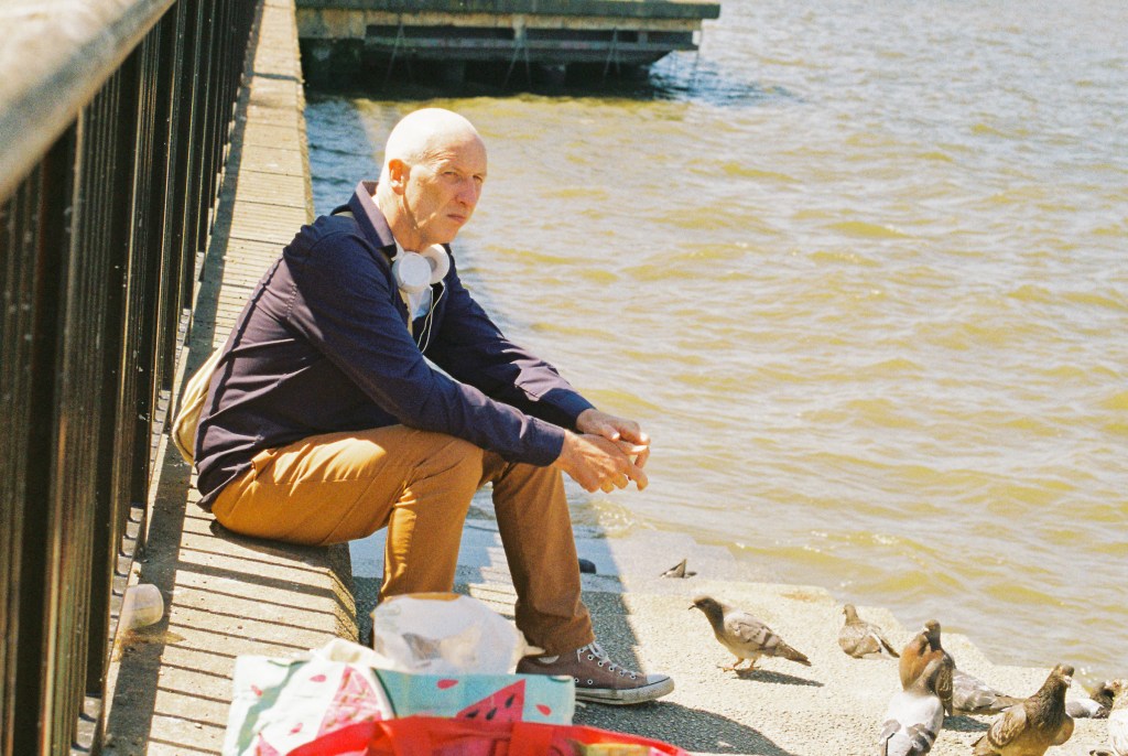 A man is seating on the Thames bank edge with pigeons in front of him