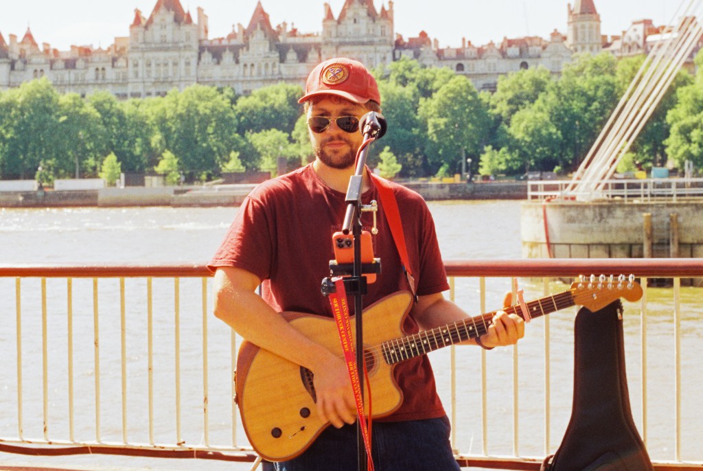 James a singer with his guitar busting on the Thames pathway in front of the Tate Modern